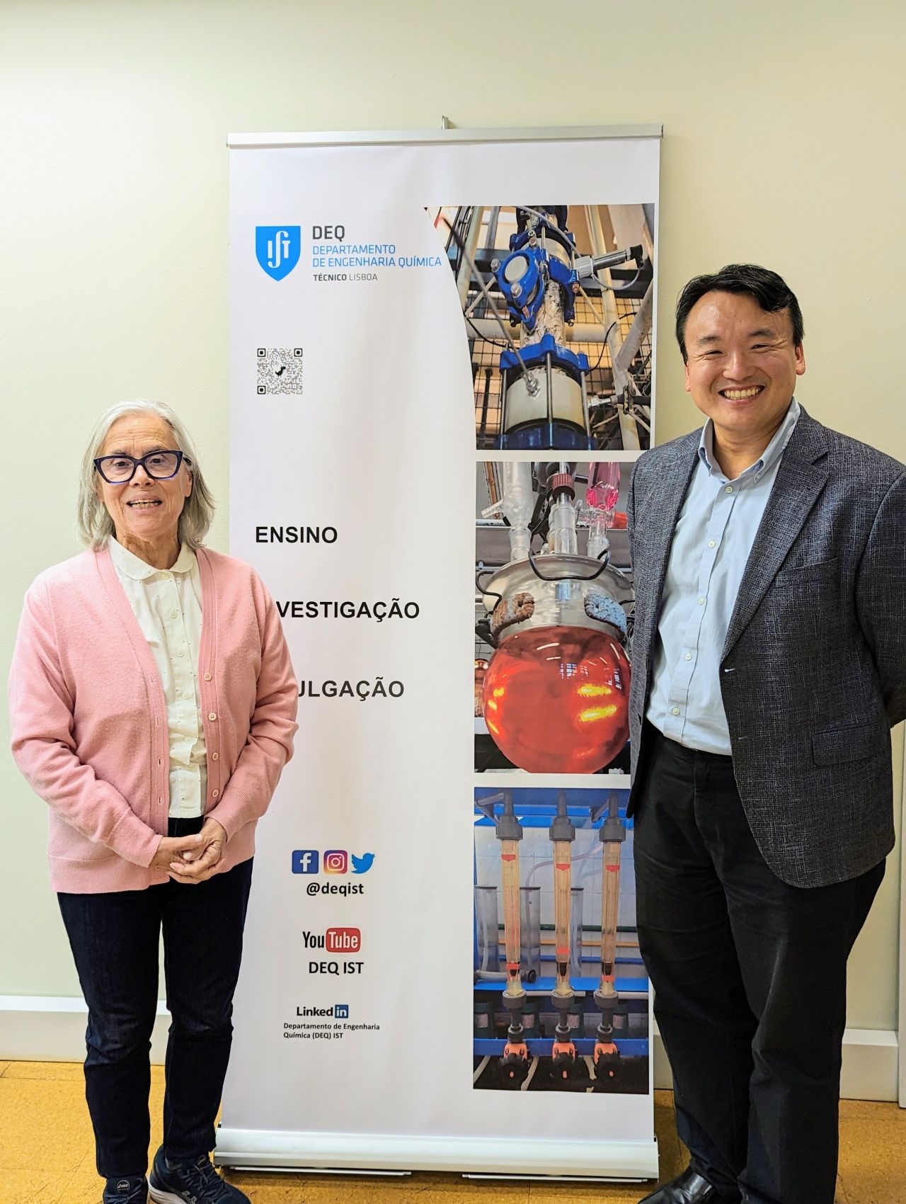 A female professor and a male professor standing in front of a banner.