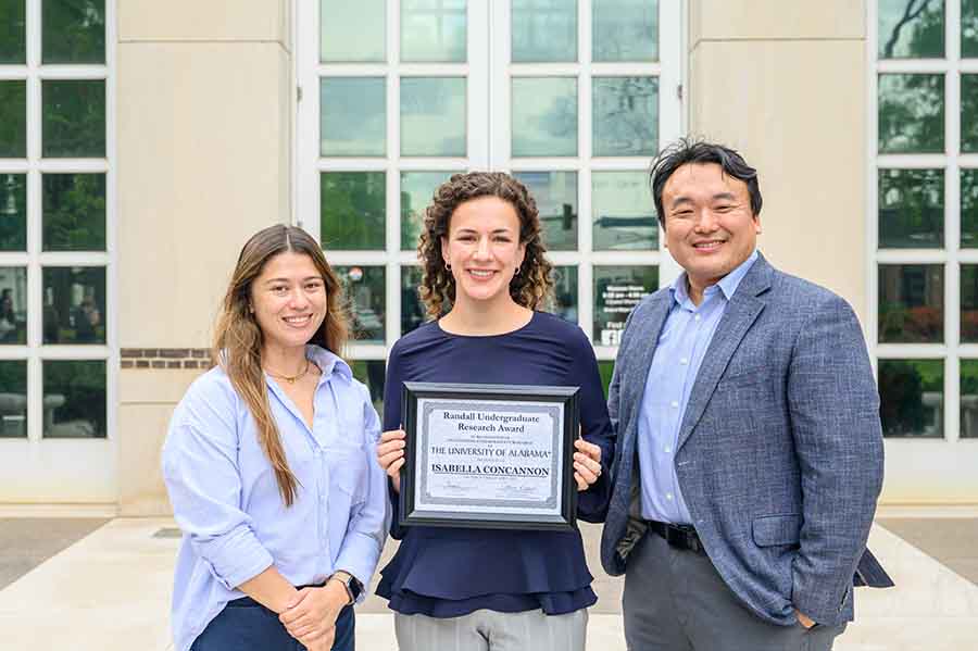 A female student holding an award plaque in the middle next to another student and a professor