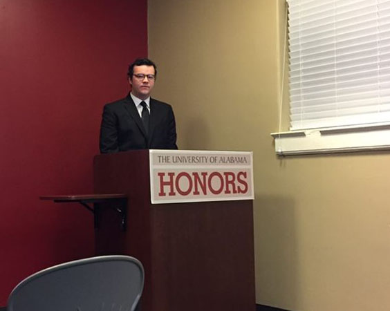 A male student standing behind a lectern labeled 'The University of Alabama Honors'