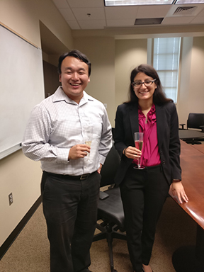 A smiling male professor and a smiling female student holding champagne glasses