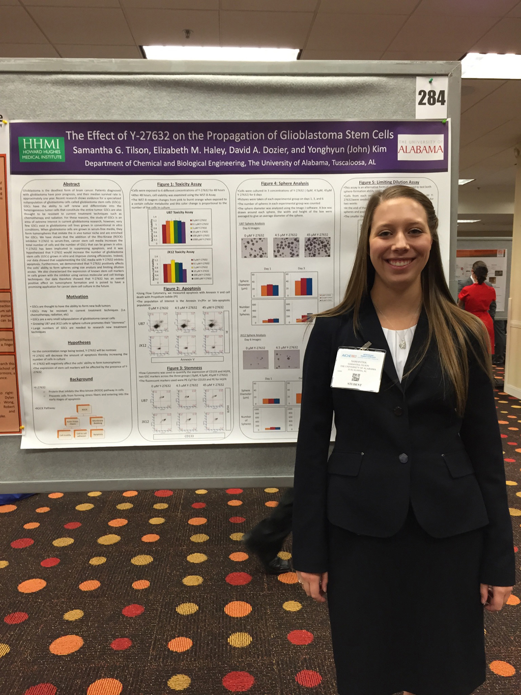 A female student in business attire standing in front of a research poster