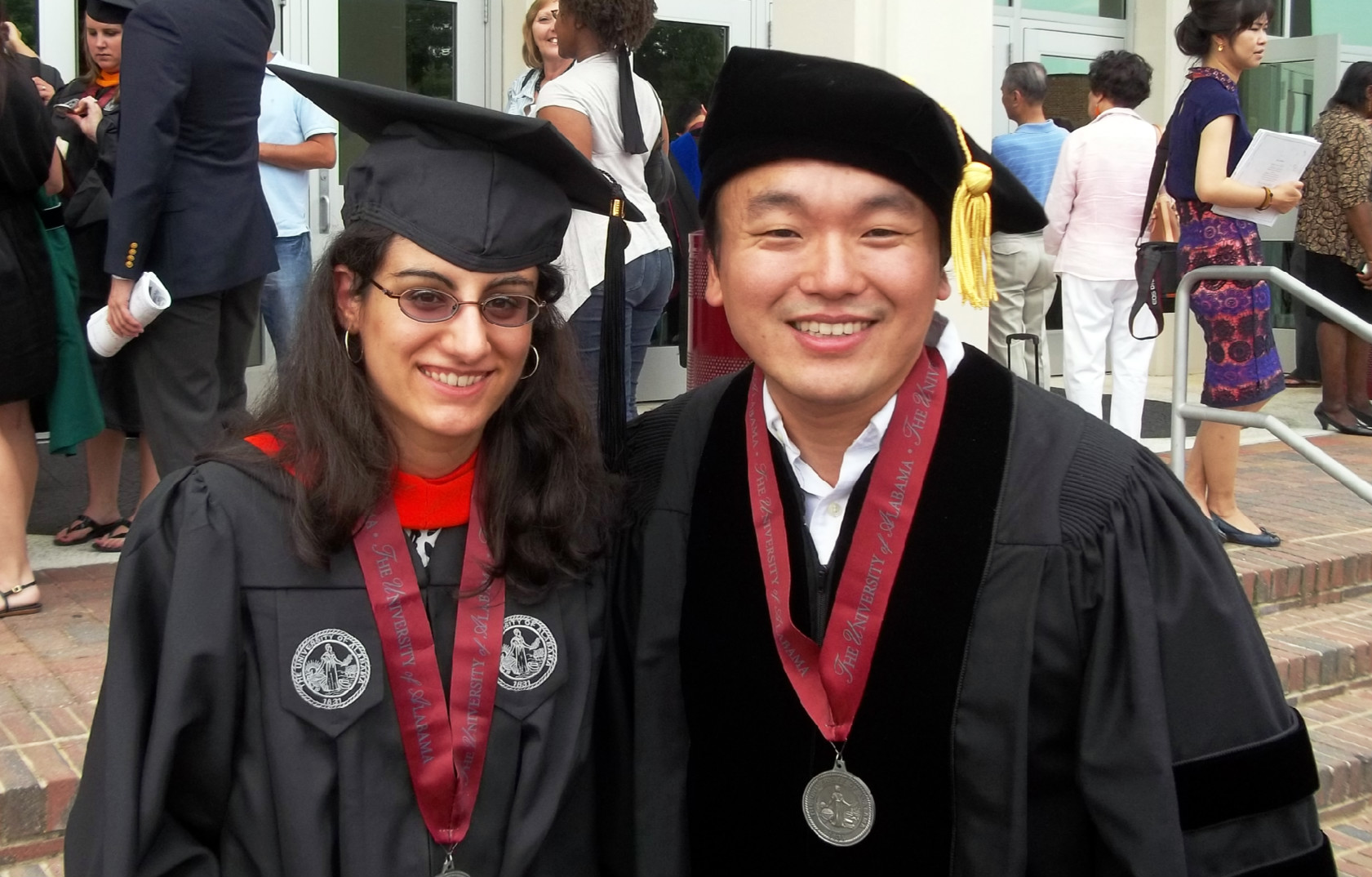 Female student with black graduation gown and cap standing next to a male professor in academic regalia