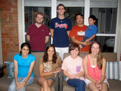 Four people standing behind four people sitting in front of a home window