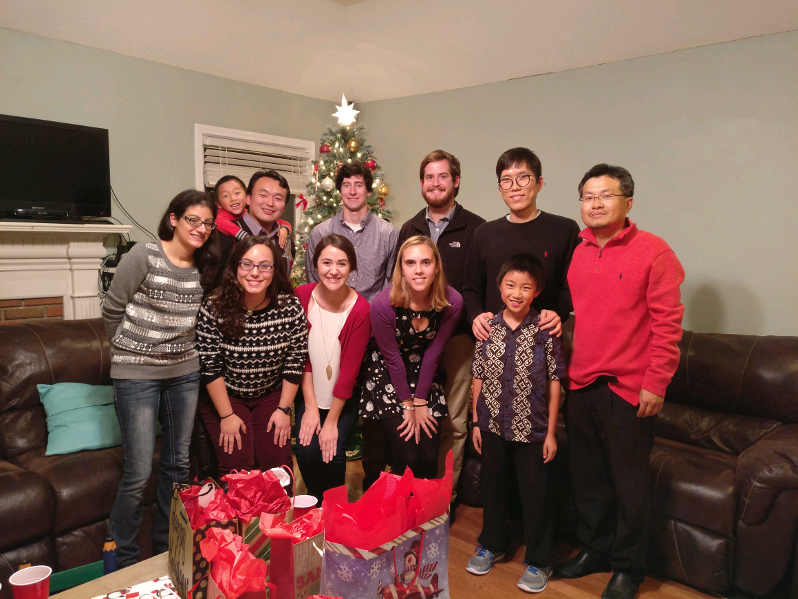 A group of 11 people standing behind red Christmas gift bags and in front of a Christmas tree