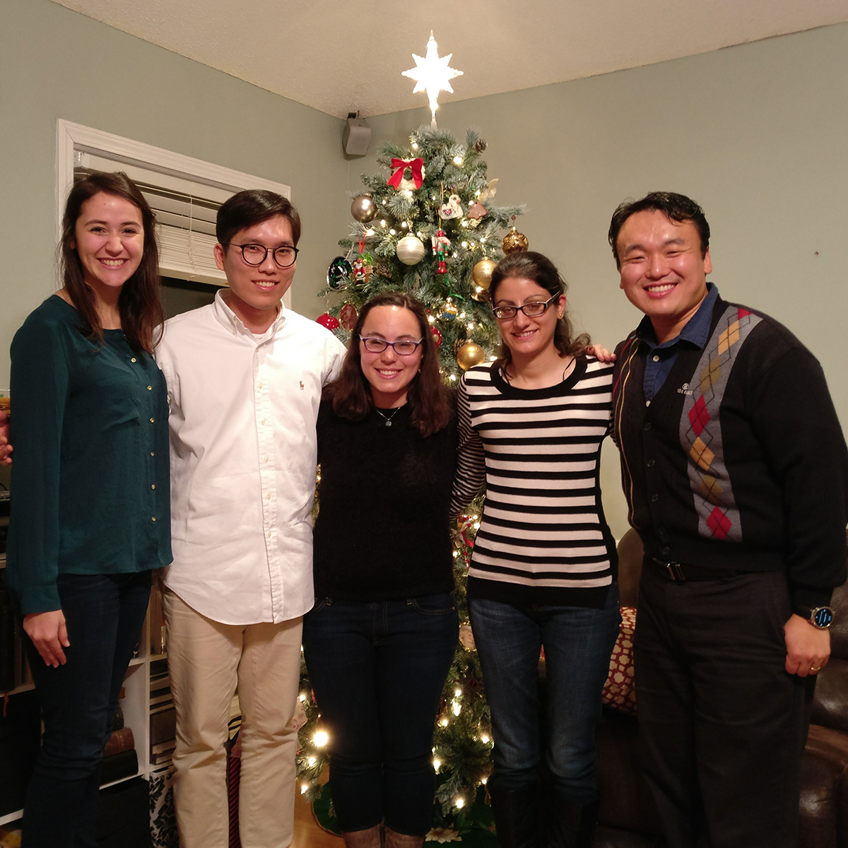 Four students and a male professor standing in front of a Christmas tree