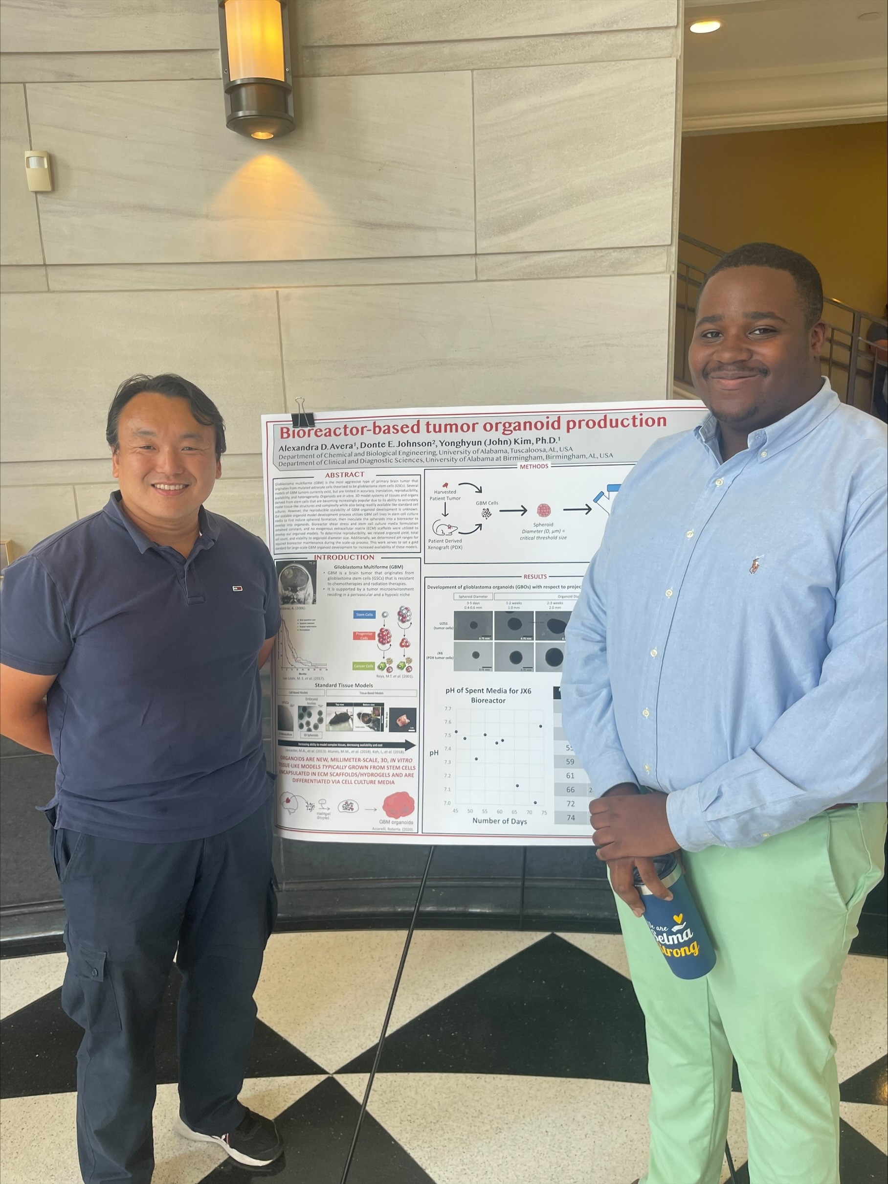 A male professor and a male student standing in front of a research poster
