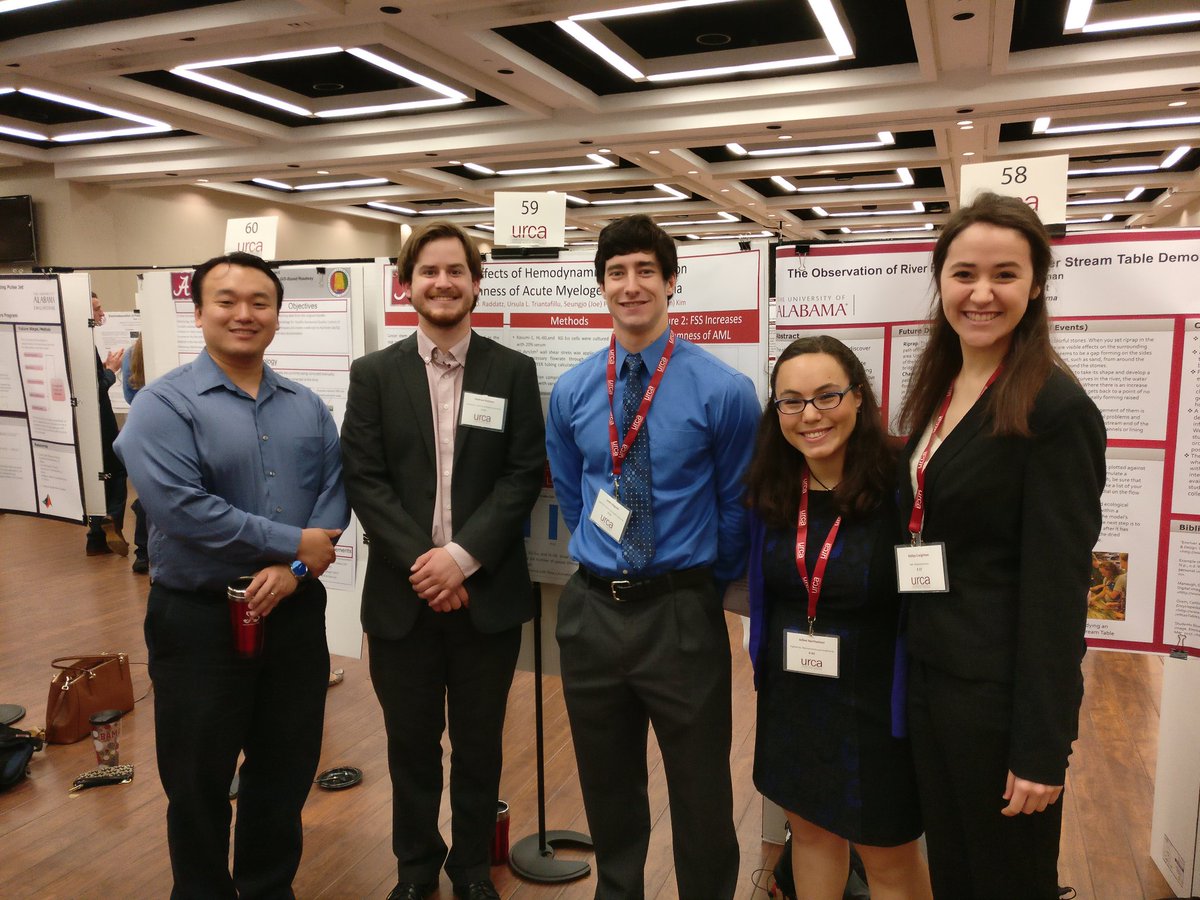 A male professor and four students standing in front of posters at a conference