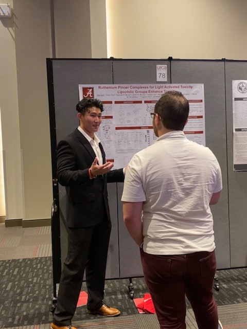 One male student standing in front of a poster and speaking to a male audience