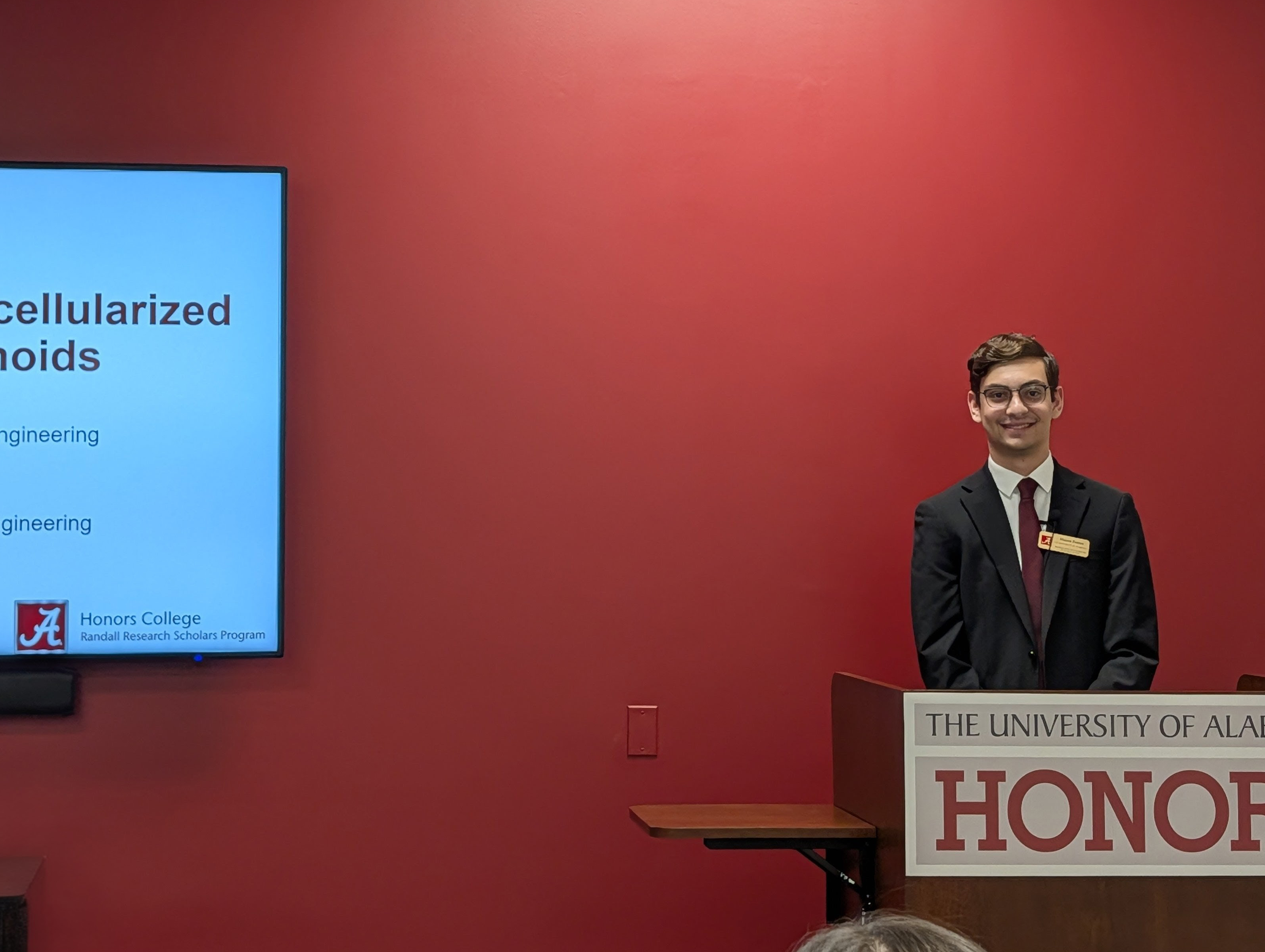 One male student presenting in front of a red wall behind a podium