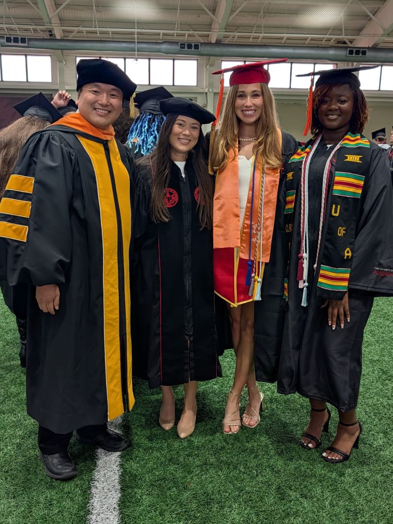 A professor and three students in graduation regalia