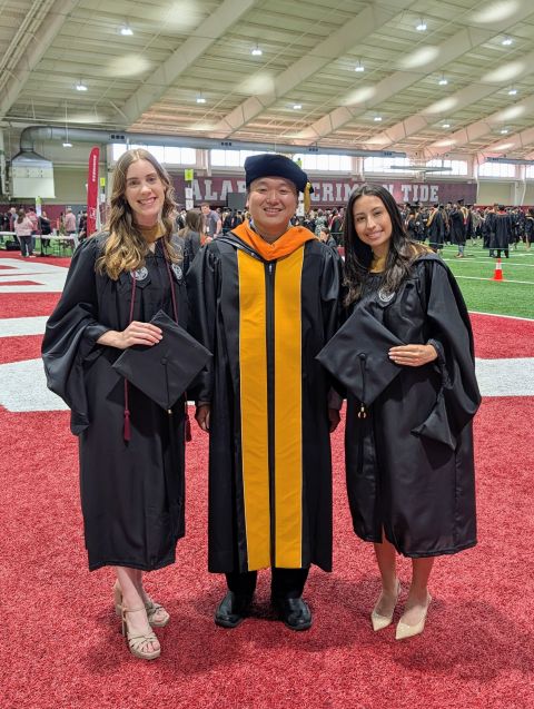 A professor and two students in graduation regalia