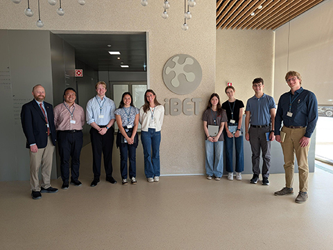 A group photo of professors and students in front of the iBET logo in a building lobby